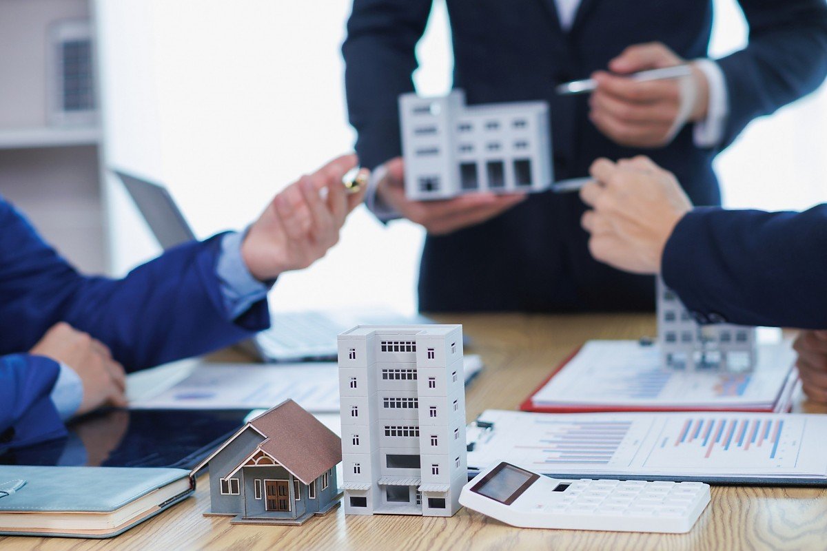 Immobilienmakler und Architekten diskutieren Neubau- und Sanierungsprojekt mit Modellen und Bauplänen Immobilienprofis besprechen Bauprojekt mit Hausmodellen und Plänen am Konferenztisch